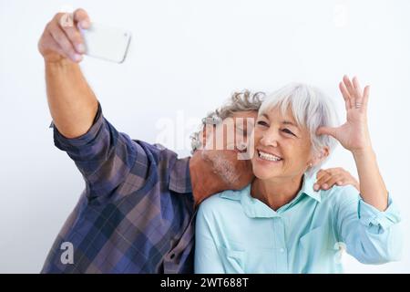 Vecchia coppia, baciati in selfie e felici insieme per post sui social media, memoria e amore con divertimento su sfondo bianco. Affetto, fiducia o lealtà con Foto Stock