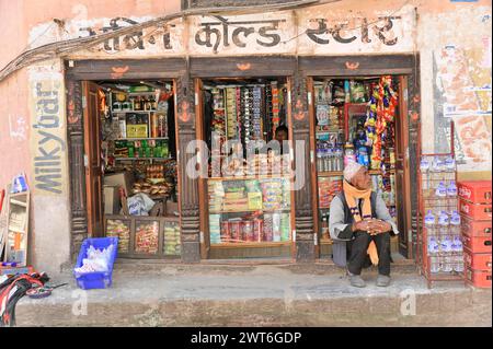 Un uomo nepalese siede accanto a un negozio tradizionale pieno di merci, la valle di Kathmandu. Kathmandu, Nepal Foto Stock