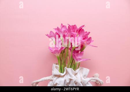 Foto dall'alto di un bouquet di gigli rosa in una borsa a cordoncino sfondo rosa isolato con spazio immacolato. Fiori primaverili su un piatto rosa. Biglietto d'auguri, holi Foto Stock