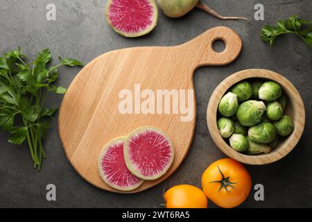 Composizione piatta con tagliere in legno e prodotti su tavolo con trama scura Foto Stock