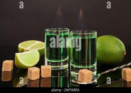 Assenzio fumante nei bicchieri da shot, zucchero di canna, lime e cucchiaio sul tavolo a specchio. Bevanda alcolica Foto Stock