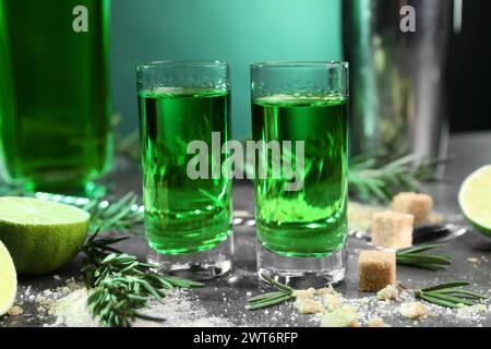 Absinthe in bicchieri da shot, zucchero di canna, rosmarino e lime su tavolo grigio, primo piano. Bevanda alcolica Foto Stock