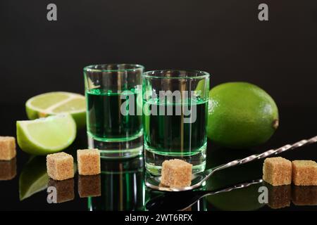 Absinthe in bicchieri da shot, zucchero di canna, lime e cucchiaio sul tavolo a specchio. Bevanda alcolica Foto Stock