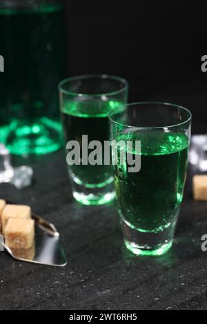 Absinthe in bicchieri da shot, cucchiaio e cubetti di zucchero di canna su un tavolo grigio, primo piano. Bevanda alcolica Foto Stock