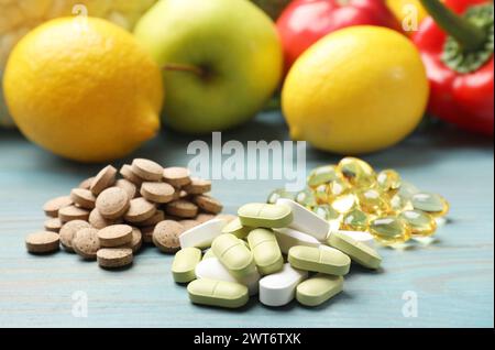 Integratori alimentari. Pile di diverse pillole vicino a prodotti alimentari su tavola di legno azzurra, primo piano Foto Stock