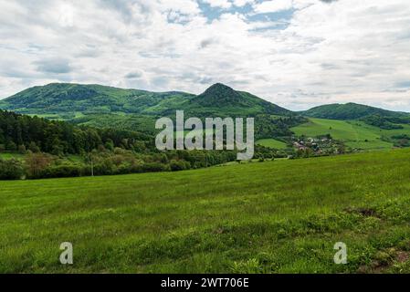 Enorme prato verde fresco, piccolo villaggio e colline ricoperte principalmente di foresta sopra - splendide montagne primaverili Starzovske vrchy in Slovacchia Foto Stock