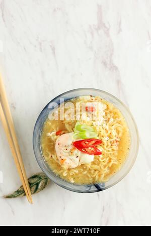 Mie Kuah Telur per Sahur nel Ramadan, zuppa istantanea di spaghetti servita in ciotola di vetro con uovo in camicia e peperoncino. Vista dall'alto su sfondo in marmo bianco. Copia SP Foto Stock