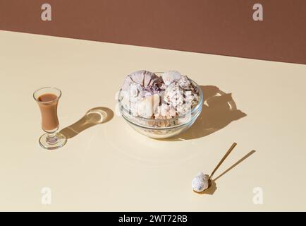 Scena estiva realizzata con una ciotola di vetro piena di conchiglie di mare e una bevanda liquorosa su sfondo beige e marrone luminoso. Concetto minimale. Foto Stock