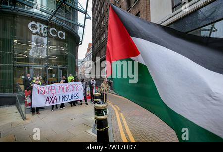 Una bandiera palestinese vola, fissata a un posto mentre i manifestanti tengono uno striscione che dice ëIsrael omicidi, AXA Insuresí durante la manifestazione. I manifestanti del fronte Giovanile per la Palestina (YFFP) e i loro sostenitori chiedono un boicottaggio dell'AXA, poiché affermano di investire oltre un miliardo di dollari in insediamenti illegali su quella che era una volta la terra palestinese e di tenere milioni in investimenti in tre banche israeliane. Affermano con questo sostegno finanziario che compagnie come AXA sono complici dei crimini di Israele contro i palestinesi a Gaza e altrove. Foto Stock