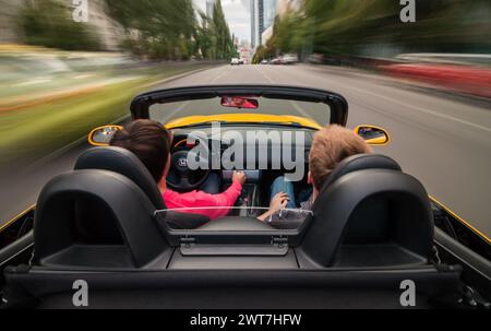 Guida veloce nel traffico urbano. Auto sportiva gialla con conducente e passeggeri che accelerano su strade trafficate in città. Senso di velocità. Foto Stock