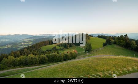 Vista dalla cima del monte Pfänder al tramonto - vista sui verdi prati alpini, la foresta di Bregenz e la gamma di alpinne del Vorarlberg sullo sfondo. Foto Stock