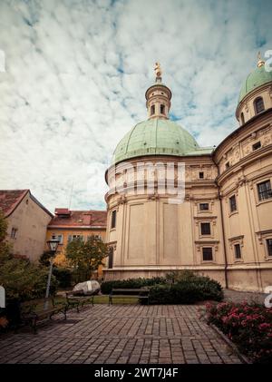 Piccolo parco con panchine vicino alla chiesa del XVII secolo - Katharinenkirche - Mausoleo dell'imperatore romano-tedesco Ferdinando II Cielo nuvoloso e luce calda. Foto Stock