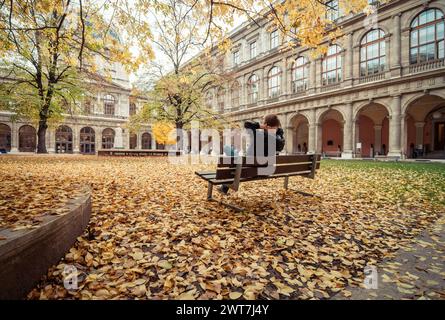 Uomo seduto su una panchina nel cortile dell'edificio principale dell'Università di Vienna. Edificio del tardo XIX secolo in stile rinascimentale italiano. Autunno. Foto Stock