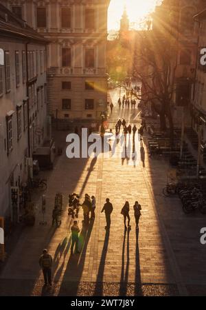 Longs ombre di pedoni su piazza Schloßbergplatz al tramonto. Vista dal Kriegssteig sul Schloßbergplatz a ovest. Immagine di contrasto Foto Stock