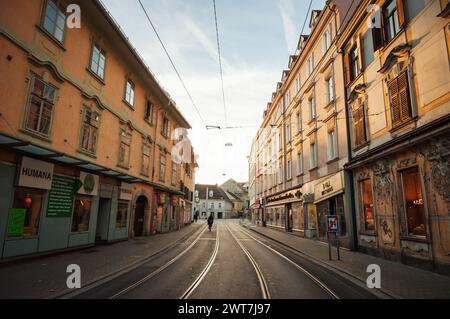 Annenstrasse la sera. Strada vuota nella città vecchia di Graz con un ciclista, raggi di sole tramontare sulle facciate degli edifici lungo la linea del tram. Foto Stock