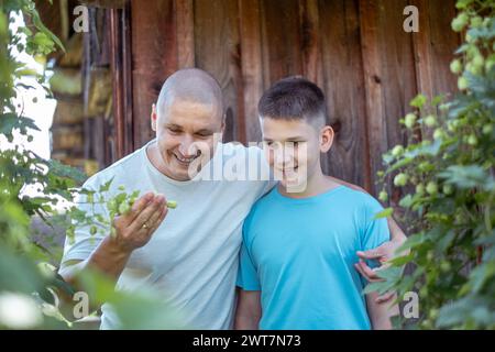 Un uomo e un ragazzo, padre e figlio, condividono un momento di gioia mentre esaminano le piante in un giardino su uno sfondo di legno, legano il tempo e la salute in famiglia Foto Stock