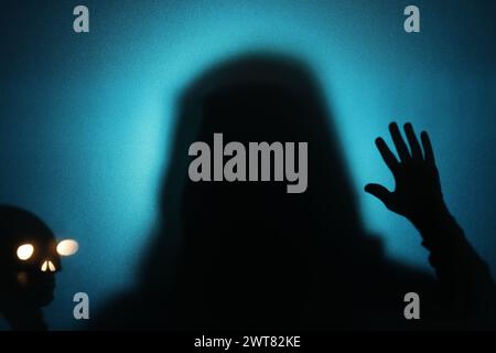 Sagoma di fantasma e cranio dietro il vetro su sfondo blu Foto Stock