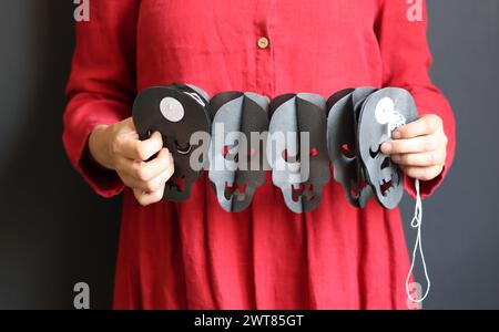 Donna in vestito rosso con il teschio garland. Foto ravvicinata delle decorazioni di Halloween. Carta fatta a mano garland per Halloween. Decorazioni natalizie. Foto Stock