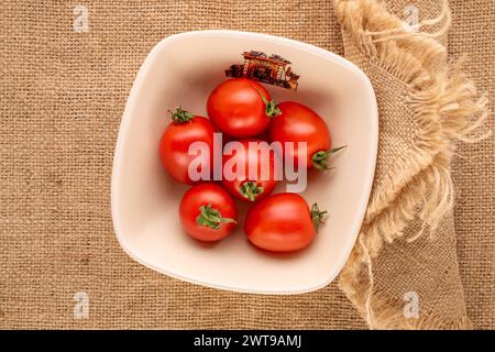 Diversi pomodori da cocktail in un piatto di ceramica su un panno di iuta, vista dall'alto. Foto Stock