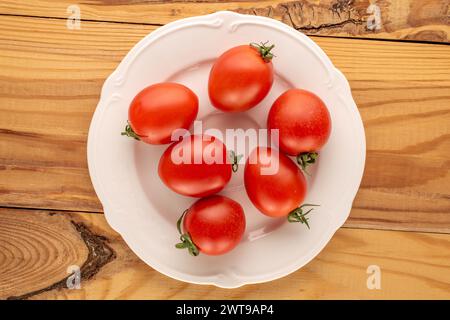 Diversi pomodori ciliegini su un piatto di ceramica bianca su un tavolo di legno, vista dall'alto macro. Foto Stock