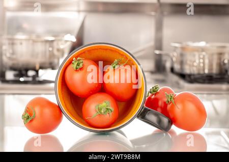 Diversi pomodori da cocktail maturi con tazza in ceramica, macro, sullo sfondo della cucina Foto Stock