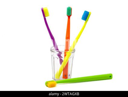 Tre spazzolini - viola, arancione e giallo con setole multicolore in una tazza trasparente su sfondo bianco. Il pennello verde Foto Stock
