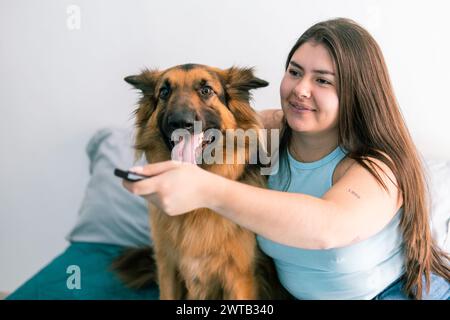 Una giovane latina con il suo cane da pastore tedesco ama guardare la TV in una camera accogliente Foto Stock