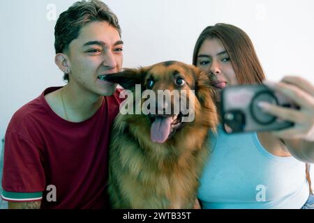 Un momento giocoso mentre una coppia latina si fa un selfie con il loro pastore tedesco, condividendo un momento di gioia Foto Stock