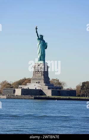 La Statua della libertà si trova in posizione dominante su un'isola sotto un cielo blu, Manhattan, Down Town, New York City, New York, Stati Uniti, Nord America Foto Stock