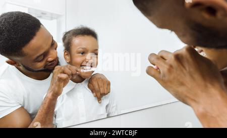 Padre premuroso che pulisce i denti della figlia in bagno Foto Stock