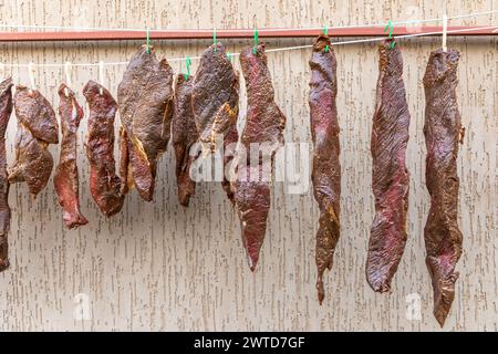 Selezione di pezzi di manzo crudi appesi all'esterno per diventare un popolare piatto sudafricano chiamato biltong. Foto Stock
