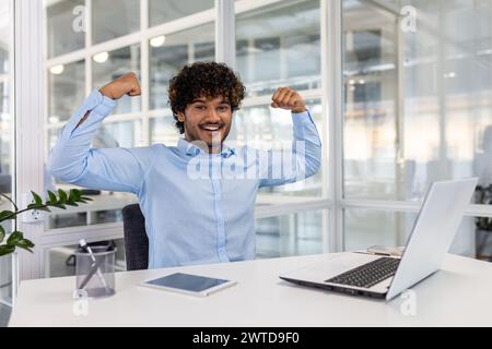 Un esuberante professionista alza trionfalmente il pugno in un ambiente di ufficio moderno, celebrando un successo aziendale. Foto Stock