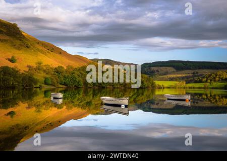 Tre barche a remi in legno si trovano immobile sullo specchio come le acque di Ullswater in una tranquilla mattina primaverile. Foto Stock