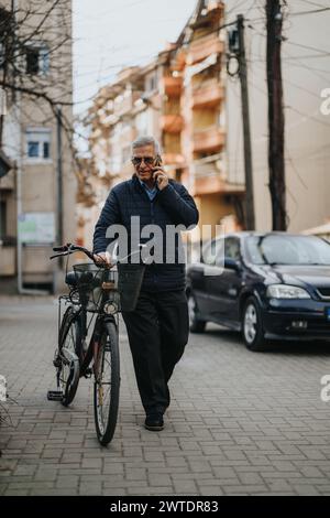 Uomo anziano con occhiali che fa una telefonata mentre cammina con la sua bicicletta in città. Foto Stock