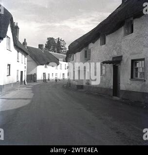 1950, storica strada inglese del Devon, mostra tradizionali cottage a schiera costruiti in pietra con tetto in paglia, Inghilterra, Regno Unito. Un cartello in alto sul muro di uno dice poi Public Telephone. Foto Stock