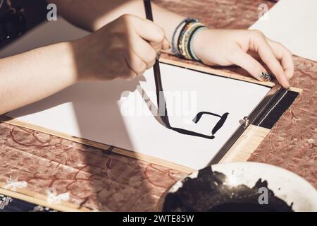 Primo piano con una mano che regge un pennello e scrive una caligrafia asiatica Foto Stock