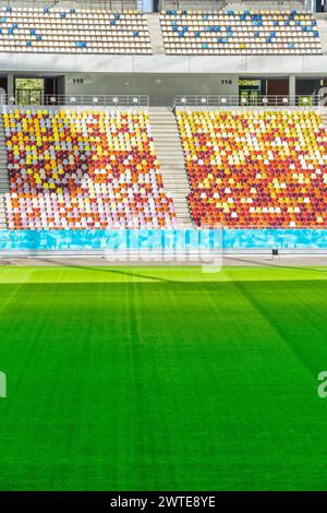Stadio vuoto con sedie colorate in tribuna e prato verde Foto Stock