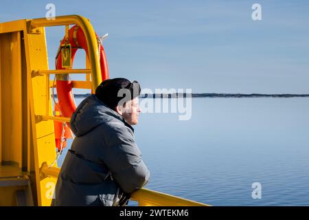 CONTEMPLAZIONE, TRAGHETTO PER L'ARCIPELAGO, MS UTÖ, ARCIPELAGO DI TURKU: Un uomo con un cappello da pelliccia è immerso nella contemplazione del bellissimo arcipelago di Turku in una fresca giornata invernale di sole dal traghetto gratuito MS Utö. INFO: L'arcipelago di Turku, situato nel Mar Baltico al largo della costa sud-occidentale della Finlandia, comprende migliaia di isole e isolotti. I suoi paesaggi pittoreschi, punteggiati da pittoreschi villaggi e monumenti storici, attraggono visitatori alla ricerca di tranquillità, avventure all'aperto e fascino marittimo. Foto Stock