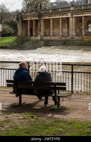 Vista posteriore di una coppia anziana seduta su una panchina, ammirando un fiume panoramico in Bath, regno unito Foto Stock