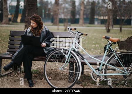 Elegante giovane donna d'affari che lavora su un computer portatile seduto sulla panca del parco Foto Stock