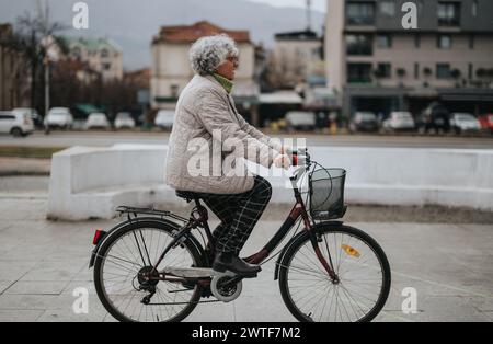 Donna anziana attiva in bicicletta in un ambiente urbano, che mette in mostra uno stile di vita sano e la mobilità urbana Foto Stock