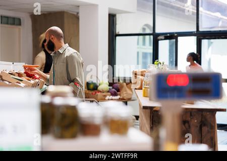 Uomo arabo che tiene e guarda la carota fresca allo stand di verdure. Il cliente medio-orientale sembra trovarsi in un negozio ecologico e alla ricerca di cibo che sostenga uno stile di vita sano. Foto Stock