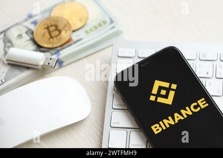 KIEV, UCRAINA - 15 MARZO 2024 Logo Binance sullo schermo dell'iPhone su tastiera bianca con denaro e bitcoin. Portale di scambio di criptovalute Foto Stock