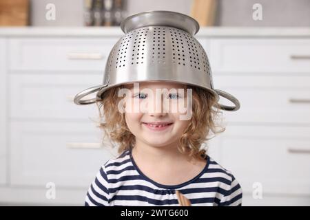 Una bambina carina con il colino sulla testa in cucina Foto Stock