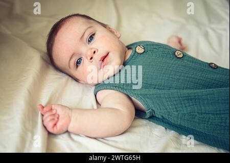 Un bambino appena nato simpatico e simpatico che si sdraia tranquillamente su lenzuola beige nel letto o nella culla. Modello di imballaggio per prodotti per bambini. Bambino sano, concetto di ospedale e maternità felice. Neonato. Asilo nido. Foto Stock