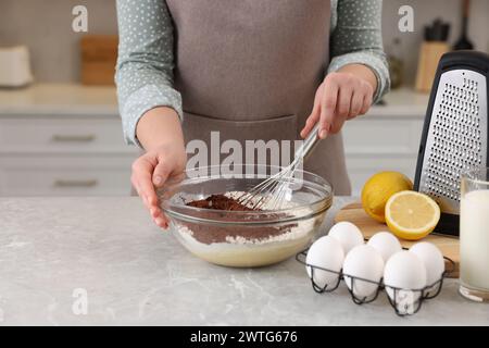 Donna che prepara l'impasto al cioccolato con la frusta nel recipiente al tavolo di marmo grigio, primo piano Foto Stock