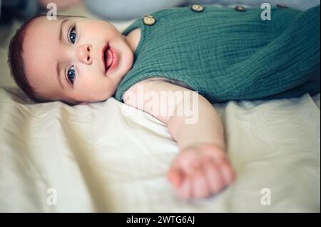 Un bambino appena nato simpatico e simpatico che si sdraia tranquillamente su lenzuola beige nel letto o nella culla. Modello di imballaggio per prodotti per bambini. Bambino sano, concetto di ospedale e maternità felice. Neonato. Asilo nido. Foto Stock