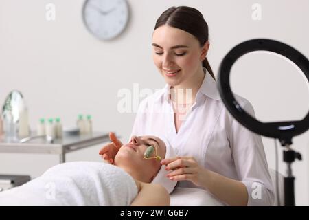 Cosmetologo che fa massaggio viso con rullo a cliente in clinica Foto Stock