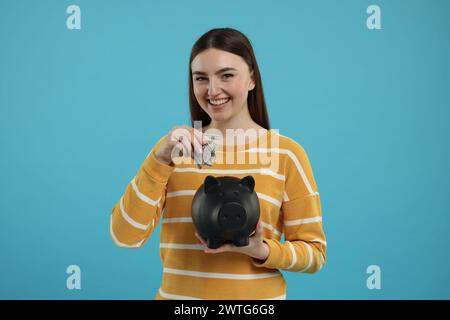 Donna felice che mette banconote da un dollaro nel salvadanaio su sfondo azzurro Foto Stock