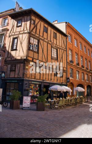 Toulouse, Haute Garonne, Francia 03.13.24 edificio storico con struttura in legno. Appartamenti in mattoni rossi in stile Toulousiane. Caffè con sedie esterne, tavoli e. Foto Stock